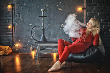 Fototapeta na wymiar girl smokes hookah / beautiful glamorous girl in red dress smokes a hookah, the sexy model in a night club smokes