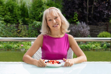 portrait beautiful, happy European blonde woman in background of wonderful garden, with plate with porridge oatmeal with berries. Concept of healthy eating, happy life, youth and longevity.