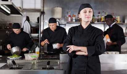 Fototapeta na wymiar Positive female cook with cooked dish in restaurant kitchen