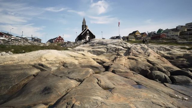 POV: Two Women Sit On Rocky Shoreline with Backdrop of Zion's Church and Interesting Architecture - Disko Bay, Greenland
