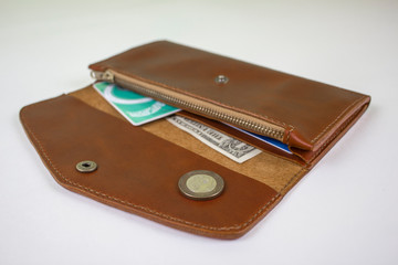 brown stitched wallet with banknotes and coins close-up on a white background