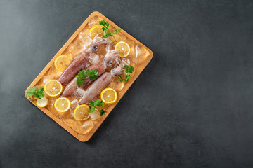 A plate of ice cubes with fresh tubules of squid and lemon slices on a black background
