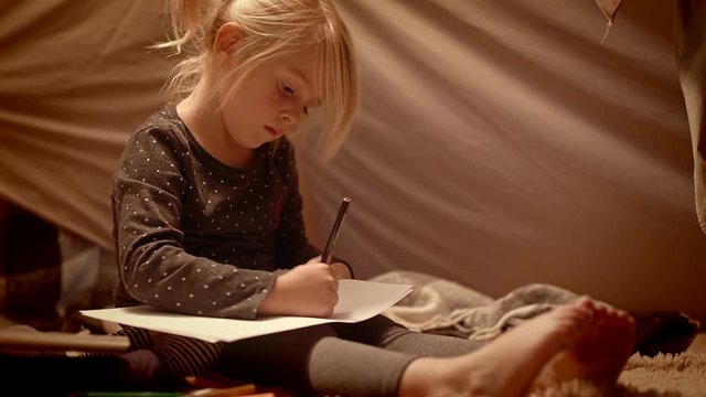 Girl draws with pencils in a decorative tent in the room at night
