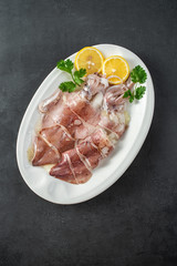 A dish of freshly cleaned platter of small tube squid and lemon slices on a black background