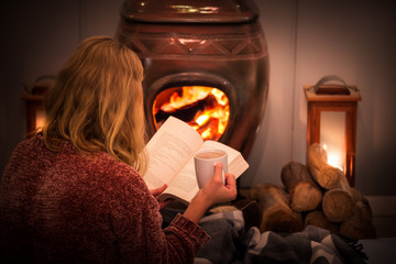 Woman/girl sitting in front of a cozy fireplace during winter under a blanket  reading a book...