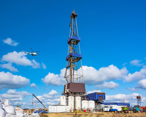 Fototapeta na wymiar In the foreground is a drilling rig for drilling oil and gas wells with various equipment and materials. In the background is a flying helicopter. Summer sunny day on the field in the far north, in th
