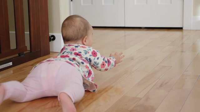An adorable girl in pink crawling on the wood kitchen floor