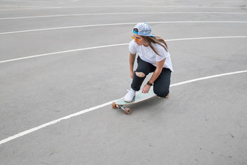 Fototapeta na wymiar Photo on side of brunette woman in baseball cap riding skateboard outdoors