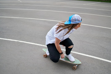 Fototapeta na wymiar Photo on side of young brunette woman in baseball cap riding skateboard outdoors