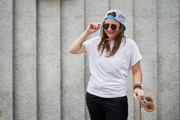 Image of happy female athlete standing with skateboard against gray granite wall