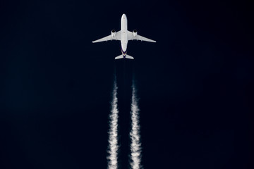 Airliner mit Kondensstreifen vor dunklem himmel 