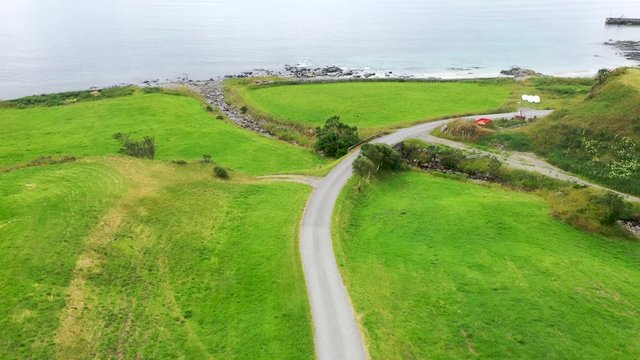 Following a country road along a shoreline towards idyllic cottages along a picturesque coast
