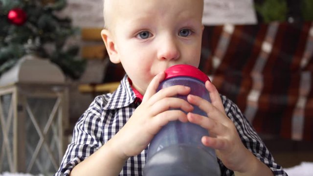 Closeup view of cute little baby boy drinking tea from special children plastic bottle holding it in small hands. Real time 4k video footage.