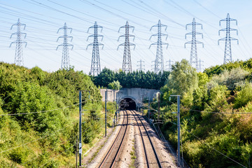 The LGV Atlantique high-speed railway passing in a tunnel under a row of electricity pylons in the suburbs of Paris, France, on a sunny summer day.