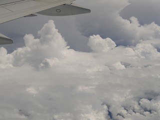Fototapeta na wymiar White storm clouds seen from an airplane window, with an airplane wing in view.