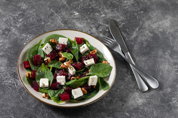 Salad with fried beets, spinach, arugula, soft goat cheese and nuts in a light plate on a background of textured concrete. Top view, copy space.