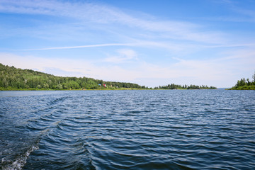 The surface of the lake water with ripples and waves against the background of wooded shores. Summer landscape in sunny weather.