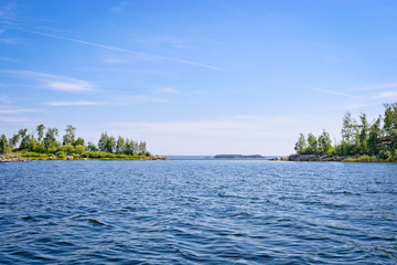 The surface of the lake is covered with ripples and waves against a rocky coast. Summer landscape in sunny weather.