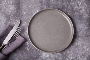 Empty gray plate and cutlery over gray concrete table. Minimalism. Copy space. Top view.