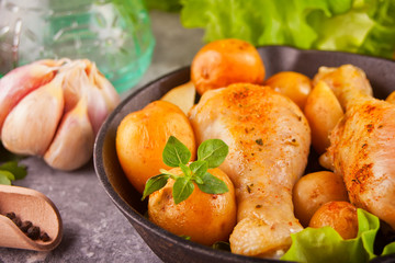 Roasted chicken legs with spices and herbs on the black pan.with vegetables on the background