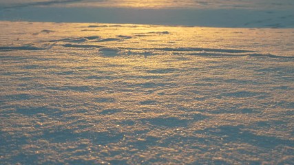 Snow field lit by evening sun, man in warm leather boots walk by. low camera position. Frosty surface, snowflakes lying on frozen field or ice