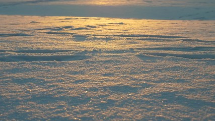 Man walk on thin snow, drag boots, snowflakes fly from bottom after steps. Close low shot of winter shoes passing by, dim evening sunlight