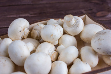 Champignon mushrooms in a wooden tray on a dark background