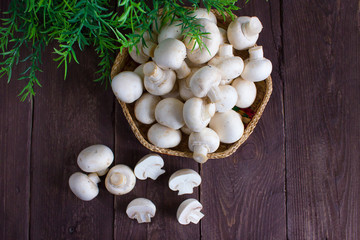 Champignon mushrooms in a wicker bowl on a dark background with a sprig of greenery