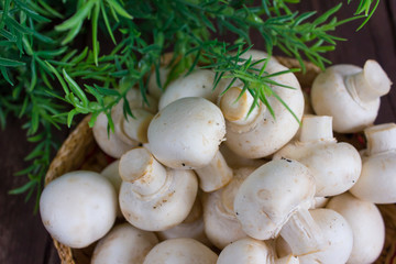 Champignon mushrooms in a wicker bowl on a dark background with a sprig of greenery