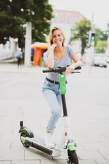 Fotobehang Junge Frau freudig lachend mit einem E-Scooter  © Wellnhofer Designs