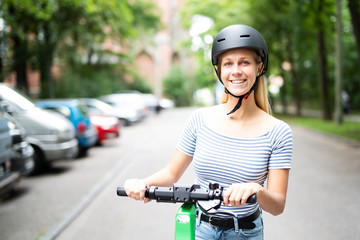 Junge Frau ist begeistert mit einem Elektroroller unterwegs, sie trägt einen Helm