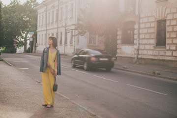 Beautiful woman in yellow jumpsuit posing on city streets.