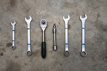 Different wrenches lying in a row on concrete floor.