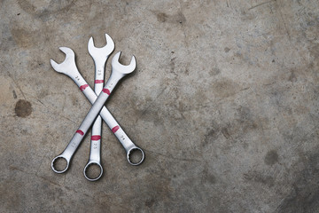 Three wrenches lying  crossed on concrete floor.