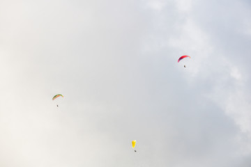 Three paragliders floating through clouds over Camps Bay, Cape Town.