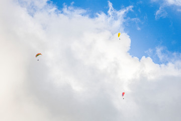Paragliders floating through clouds and blue sky over Camps Bay, Cape Town.