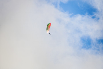 Paraglider floating through clouds and blue sky over Camps Bay, Cape Town.