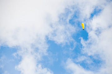 Paraglider floating through clouds and blue sky over Camps Bay, Cape Town.