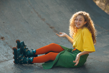 Young woman girl portrait in green and yellow clothes and orange stockings with curly hairstyle roller skating fell in skate park