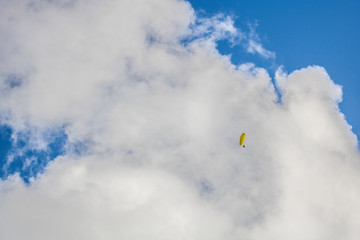 Fototapeta na wymiar Paraglider floating through clouds and blue sky over Camps Bay, Cape Town.