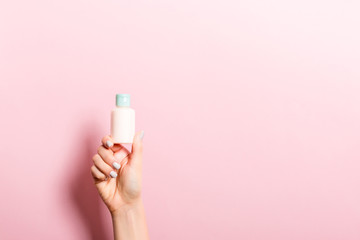 Female hand holding cream bottle of lotion isolated. Girl give tube cosmetic products on pink background