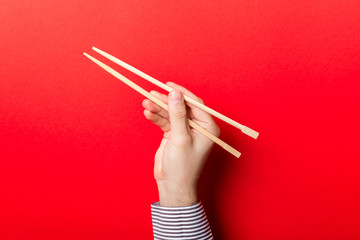 Boy's hand showing chopsticks on red background. Asian cuisine concept with empty space for your...