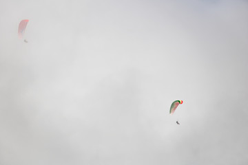 Two paragliders floating through clouds over Camps Bay, Cape Town.
