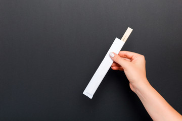 Crop image of female hand holding chopsticks on black background. Japanese food concept with copy space