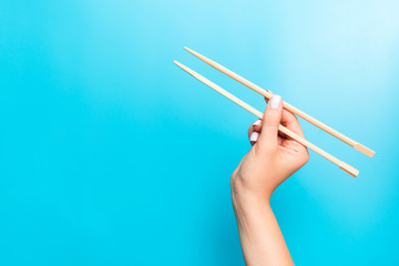 Wooden chopsticks holded with female hands on blue background. Ready for eating concepts with empty space