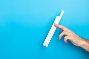 Man's hand holding chopsticks in a pack on blue background. Chinese food concept with empty space for your design
