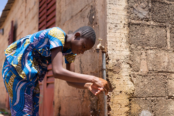 African Woman Washing Hands under Tap Outdoors