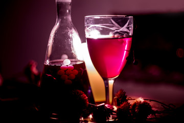 Cozy evening still life by . A glass of red wine, an old decanter, green leaves and dried flowers against a burning fire. Dark photo. The cozy atmosphere of an autumn, winter evening.