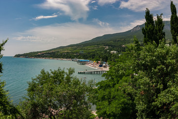 View to the city beach with umbrellas, sunbeds and people relaxing in cloudy day with mountains on the background. Black Sea.