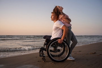 Handicapped man in wheelchair and his girlfriend on a beach at sunset